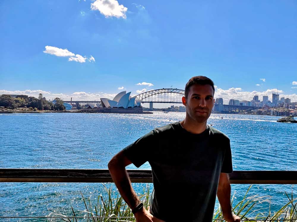 chico moreno posando para cámara y detrás la Ópera de Sydney